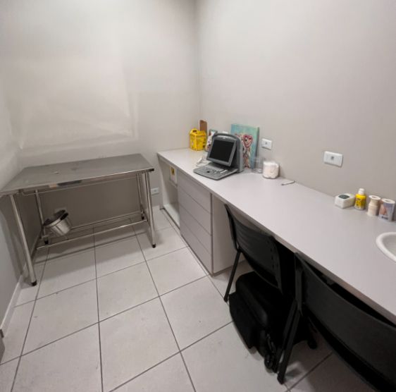 Consultório da clínica, com mesa de atendimento em inox e ultrassom portátil sobre a bancada
